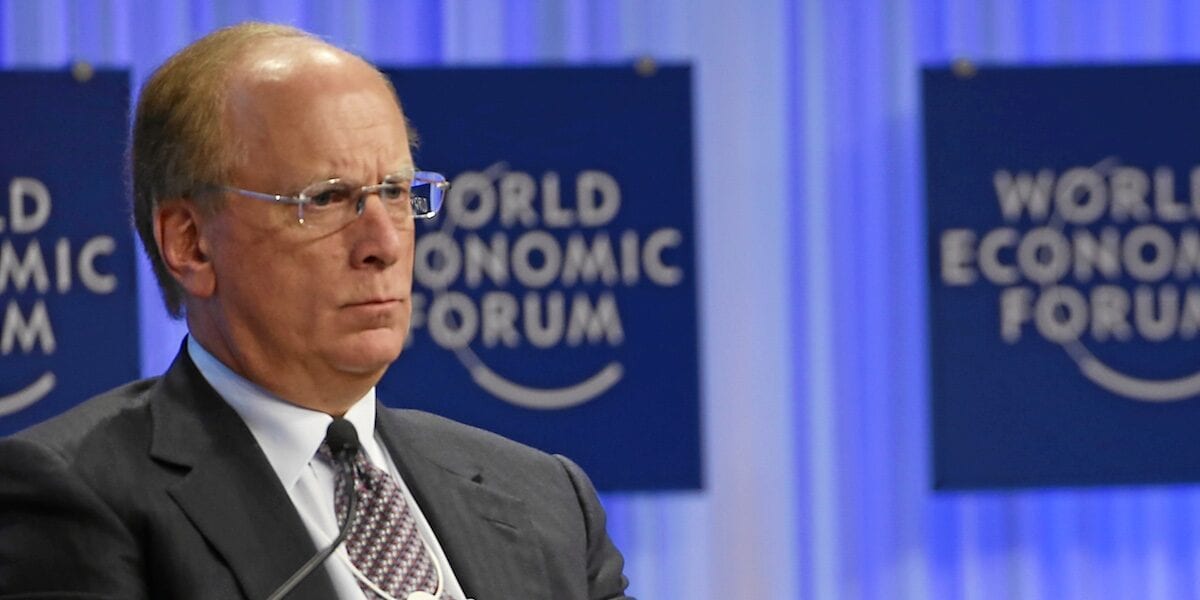 Executive in dark suit seated before World Economic Forum panel backdrop, looking off-camera