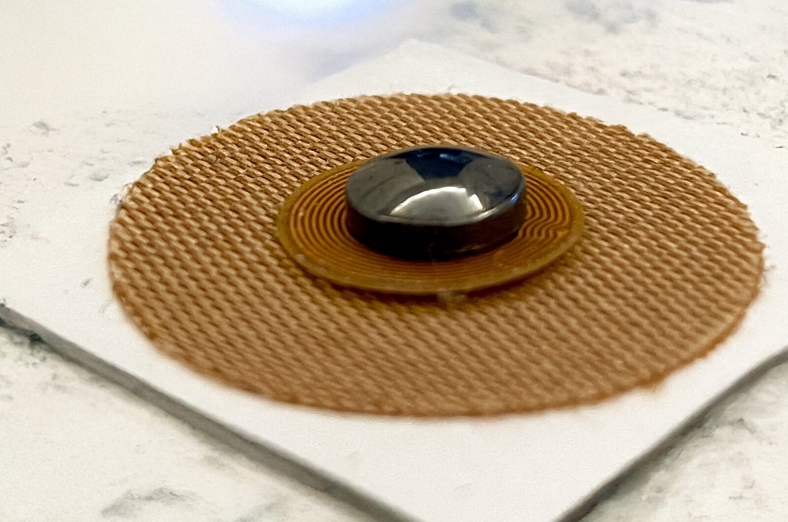 Biotag Device for Smoking Harmonization Round copper NFC antenna patch with a small black magnet at its centre on a white tile